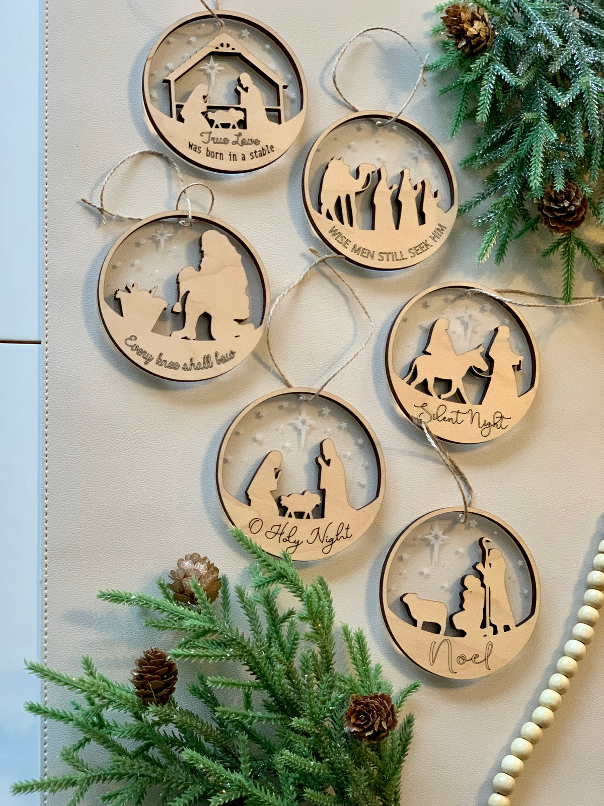 Set of two-layer wood and acrylic nativity Christmas ornaments with religious scenes and festive greenery background