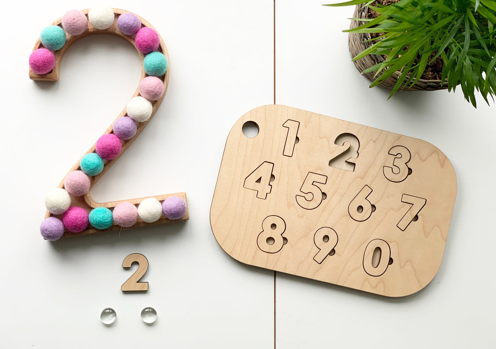 Maple plywood number puzzle with cut-out digits and colorful pom pom decorated wooden number two on white background