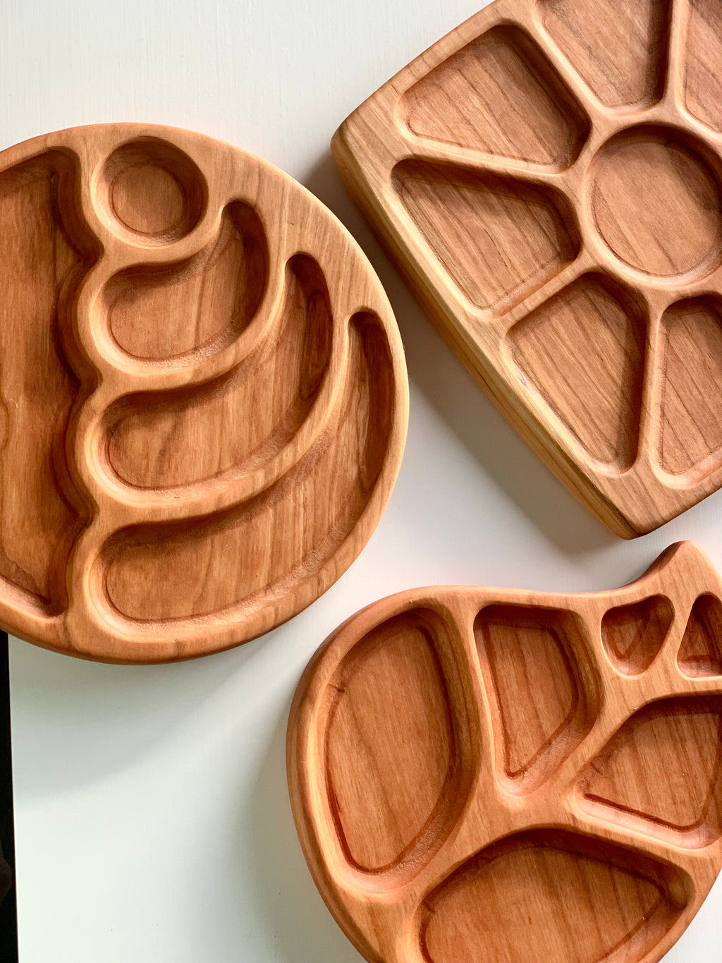 Set of natural wooden sensory trays in wave circle, floral, and fish shapes with multiple compartments on white surface