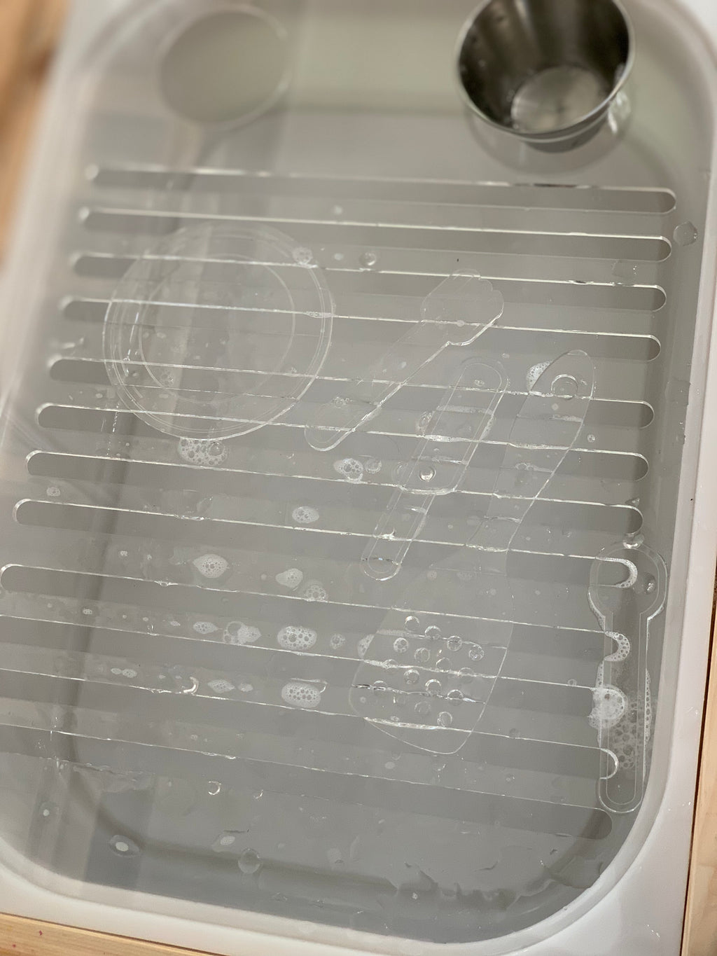 White plastic dish rack insert with water droplets and small metal cup on wooden surface