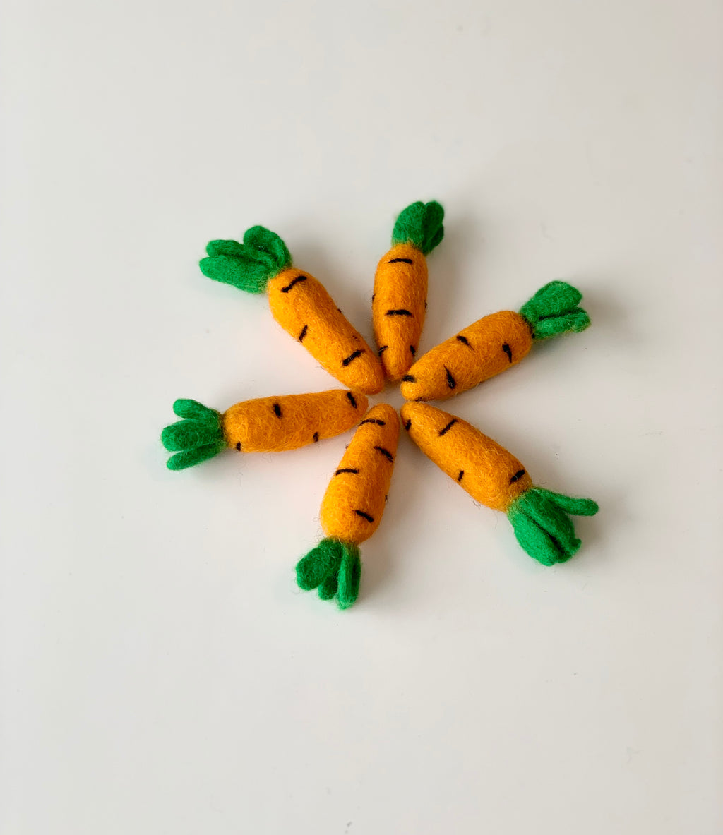 Six handmade felt carrots with green felt tops arranged in a circle on a white surface