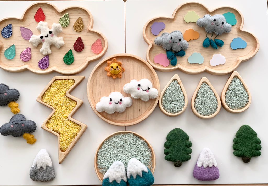 Assorted laser cut acrylic shapes and felted wool clouds arranged on wooden trays for sensory and seasonal play