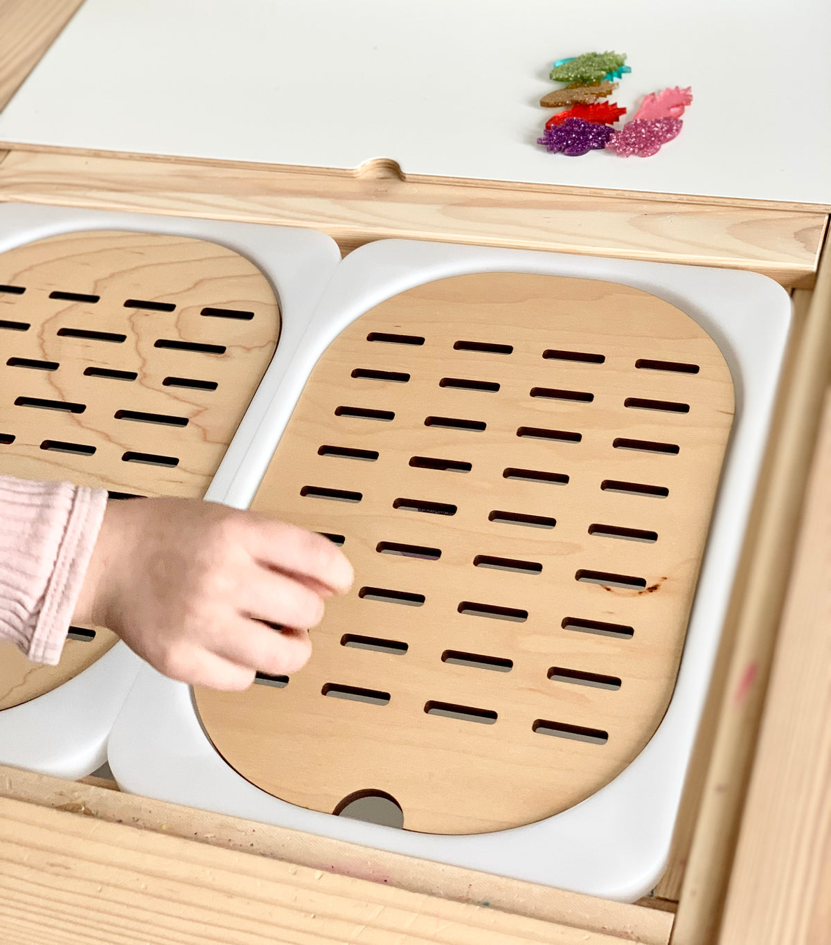 Child’s hand placing colorful resin leaves into wooden slots of Flisat table top sorter insert with white frame