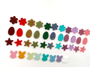 Assorted small laser cut acrylic shapes including flowers, eggs, stars, and bunny heads in multiple colors on white background
