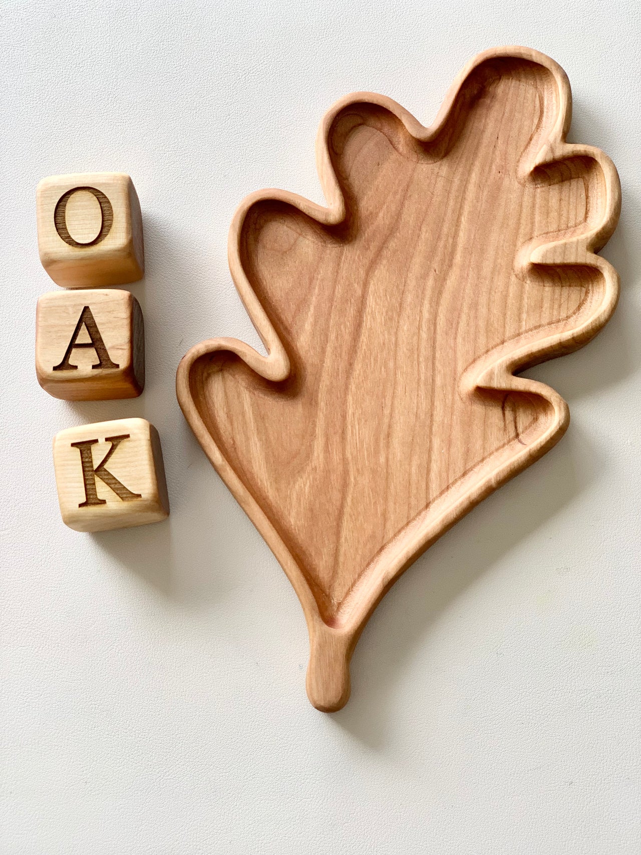 Oak leaf-shaped wooden sensory tray next to three wooden blocks spelling O A K on white surface