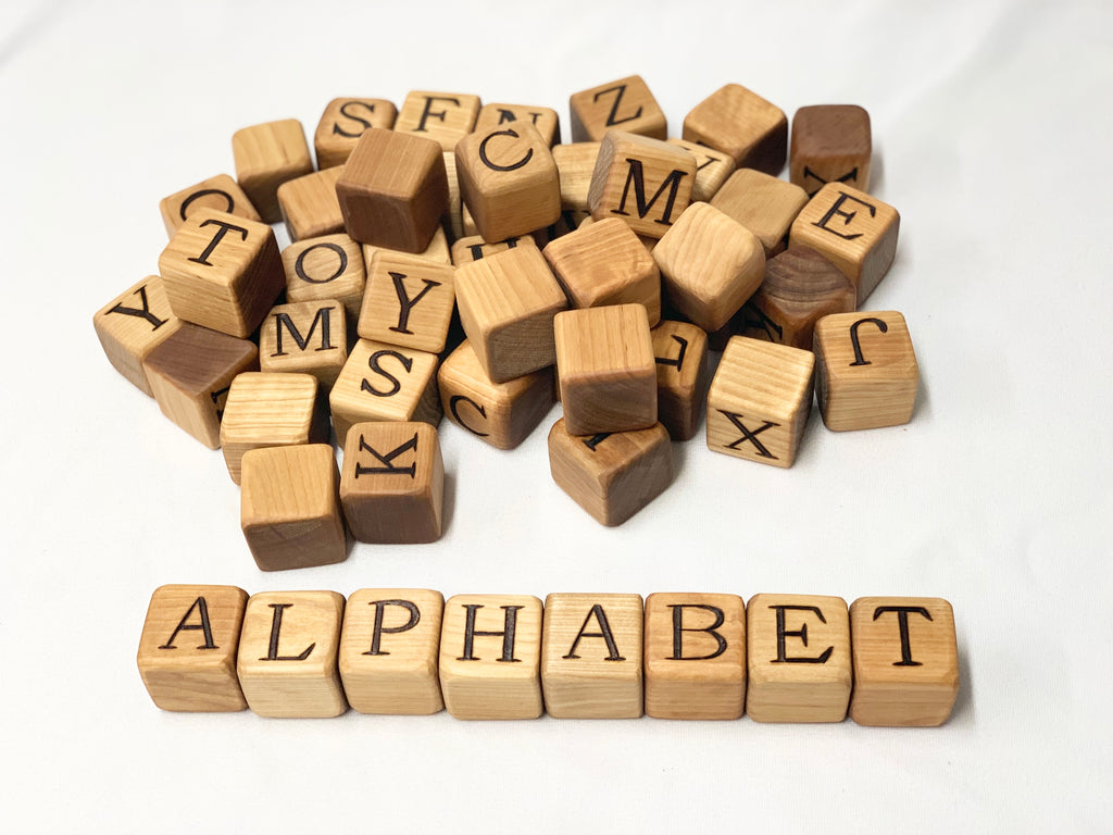 Natural wooden 2-inch alphabet blocks with engraved capital letters scattered and arranged to spell ALPHABET on white background