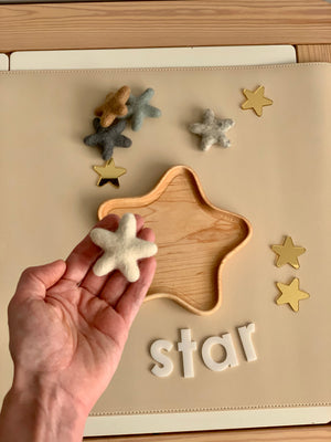 Hand holding a neutral felt star above a wooden star-shaped tray with more felt stars and white letters spelling star
