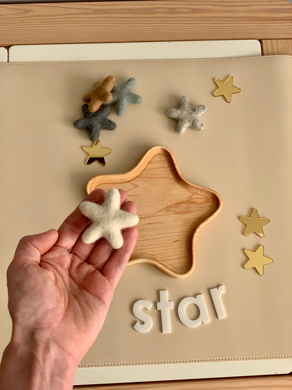 Hand holding a neutral felt star above a wooden star-shaped tray with more felt stars and white letters spelling star