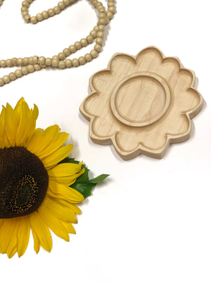 Natural unfinished wooden sunflower-shaped sensory tray next to yellow artificial sunflower and wood bead garland on white background