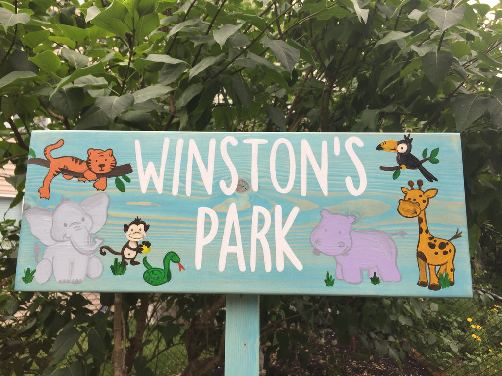 Large custom wooden garden sign painted teal with white letters and colorful cartoon jungle animals on wood grain background