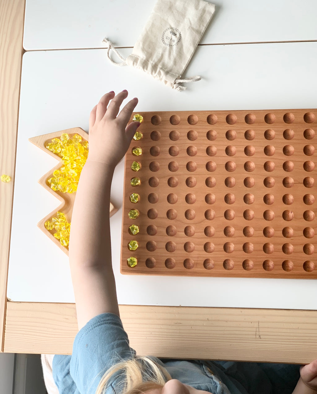 Child placing yellow translucent beads into engraved holes on a natural wooden 100 Frame Hundred Sorting Board tray