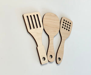 Set of three natural wooden play kitchen utensils including slotted spatula, spoon, and slotted turner on white background