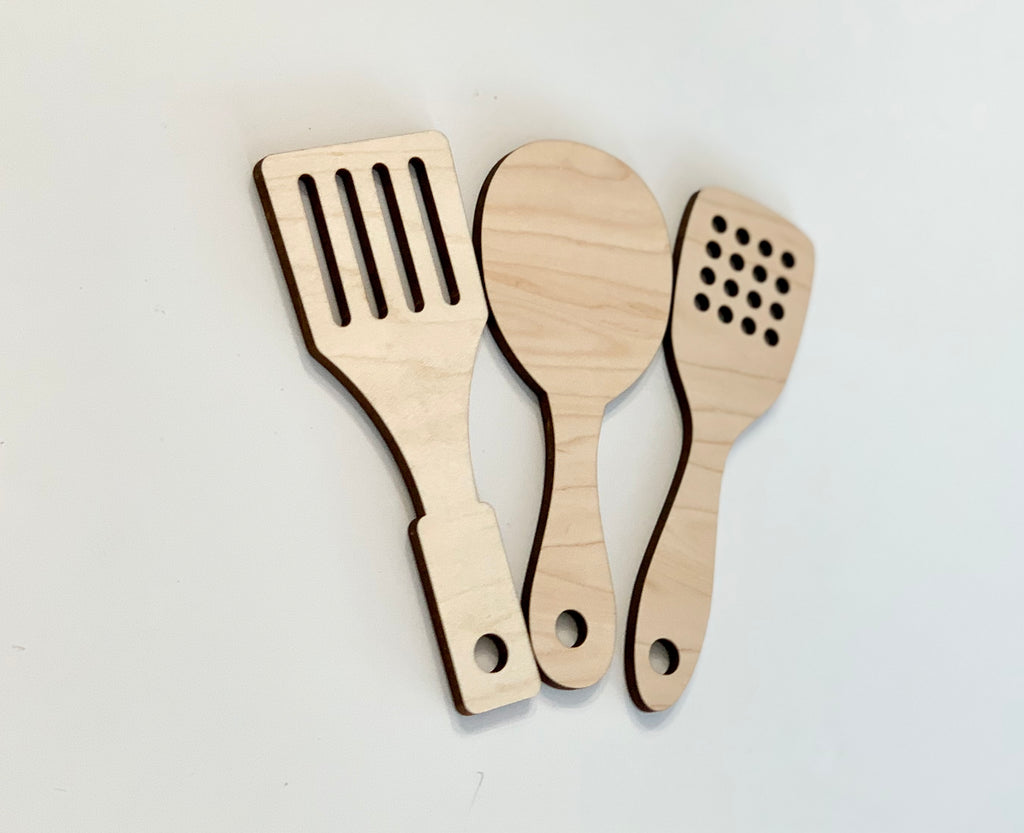 Set of three natural wooden play kitchen utensils including slotted spatula, spoon, and slotted turner on white background
