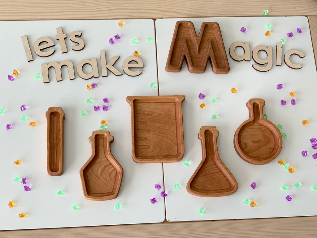 Wooden potion bottle plates shaped like scientific beakers arranged on white boards with wooden letters and colorful beads scattered around